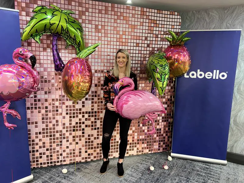 A guest holding a flamingo balloon at the Labello brand activation in front of a rose gold shimmer wall
