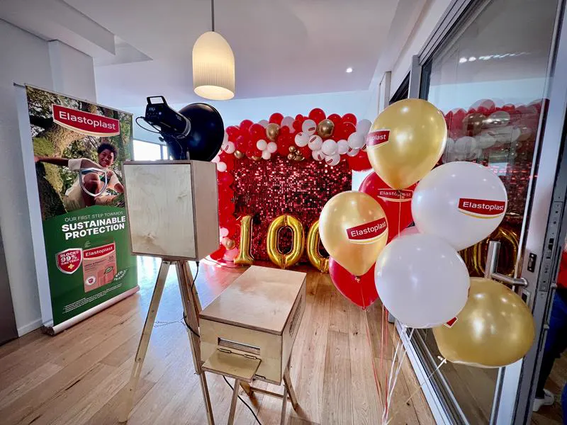 The Retrobooth at the Elastoplast 100 year celebration with a red sequin backdrop and gold balloons