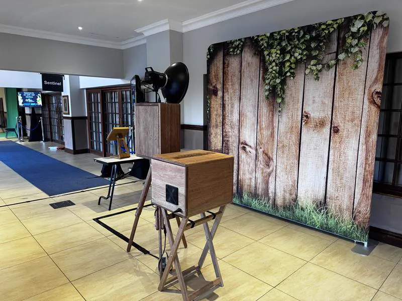 The Retrobooth and printer beside a rustic wood and ivy backdrop in a hotel foyer