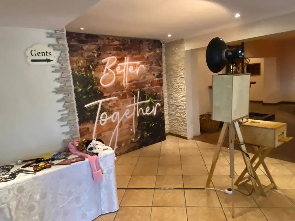 The Retrobooth beside a Better Together neon brick backdrop and a props table at a KZN wedding