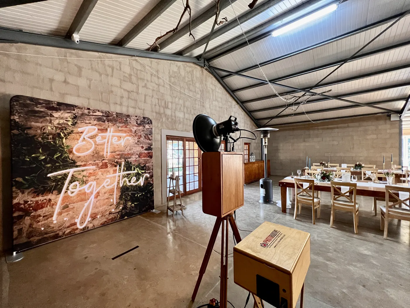 The Retrobooth facing a Better Together neon backdrop in a stone barn set for a wedding reception