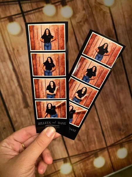 Zilleen and Dane photostrips held under festoon lights against the wood panel photobooth backdrop