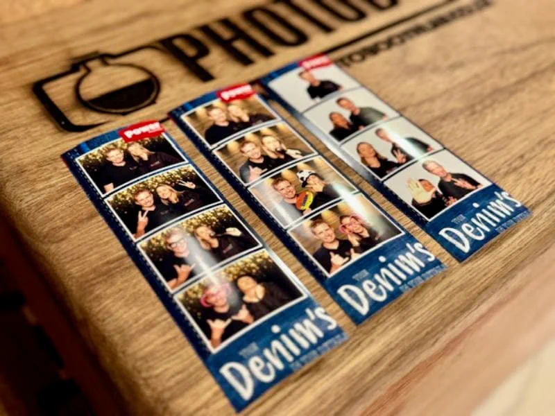 Three Denims branded photostrips laid out on the engraved wooden photobooth printer cabinet