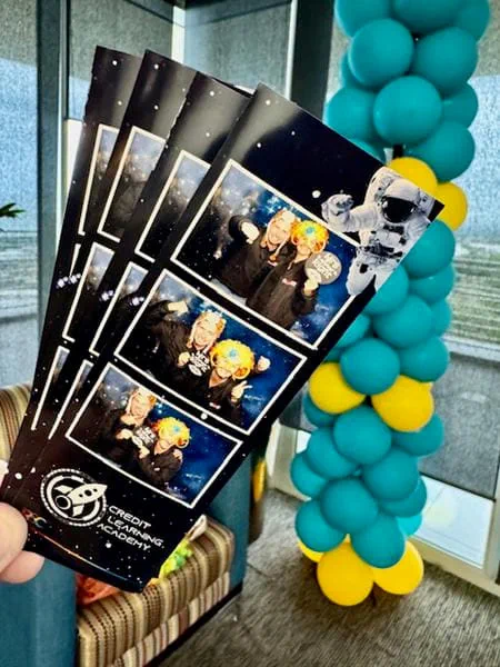 Space themed Credit Learning Academy photostrips held beside teal and yellow balloon columns at a corporate event
