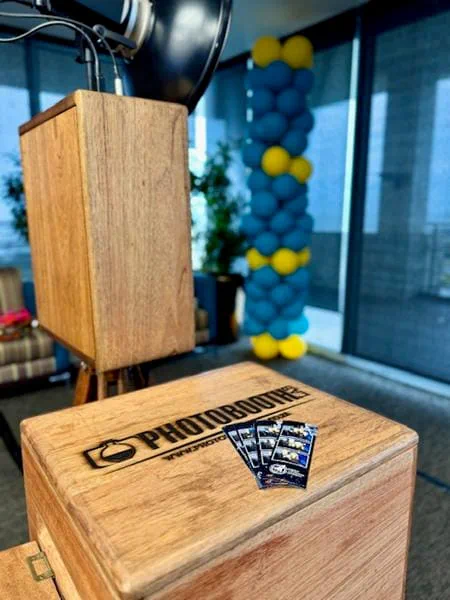 Photostrips resting on the photobooth printer box at a corporate function with a blue and yellow balloon column