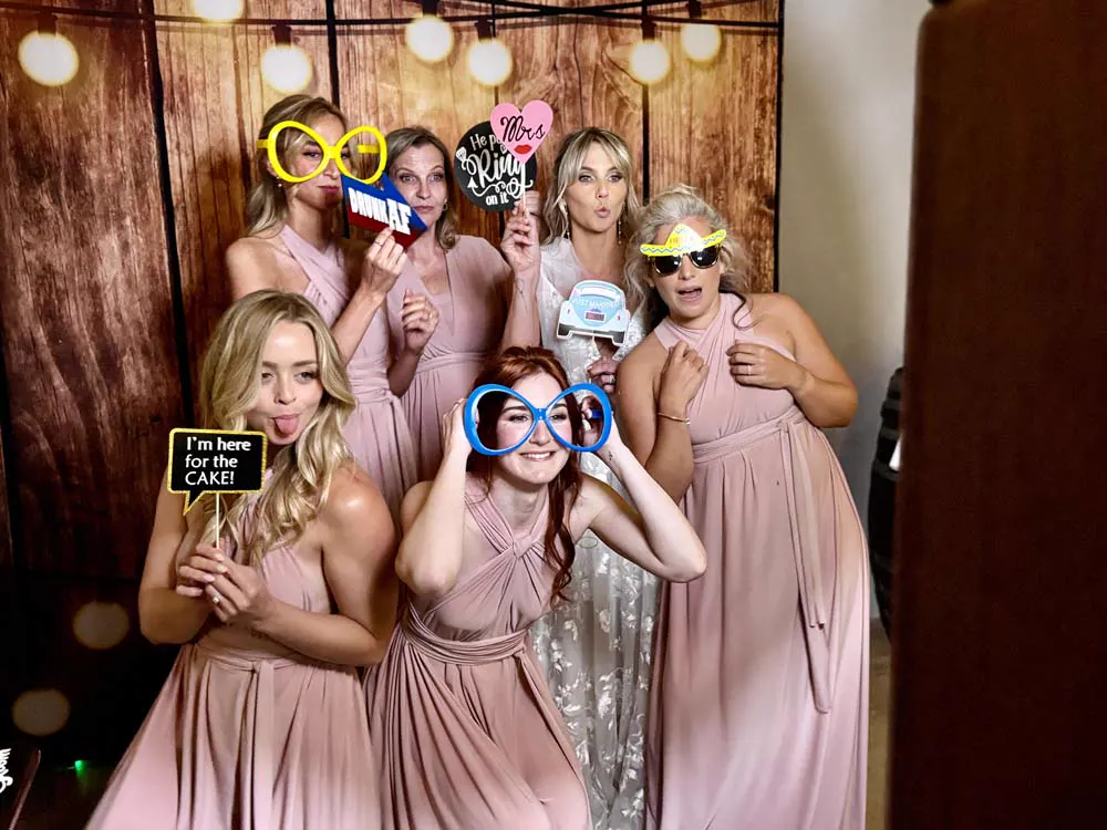 Bridesmaids in dusty pink gowns posing with props against the wood panel backdrop at a KZN wedding